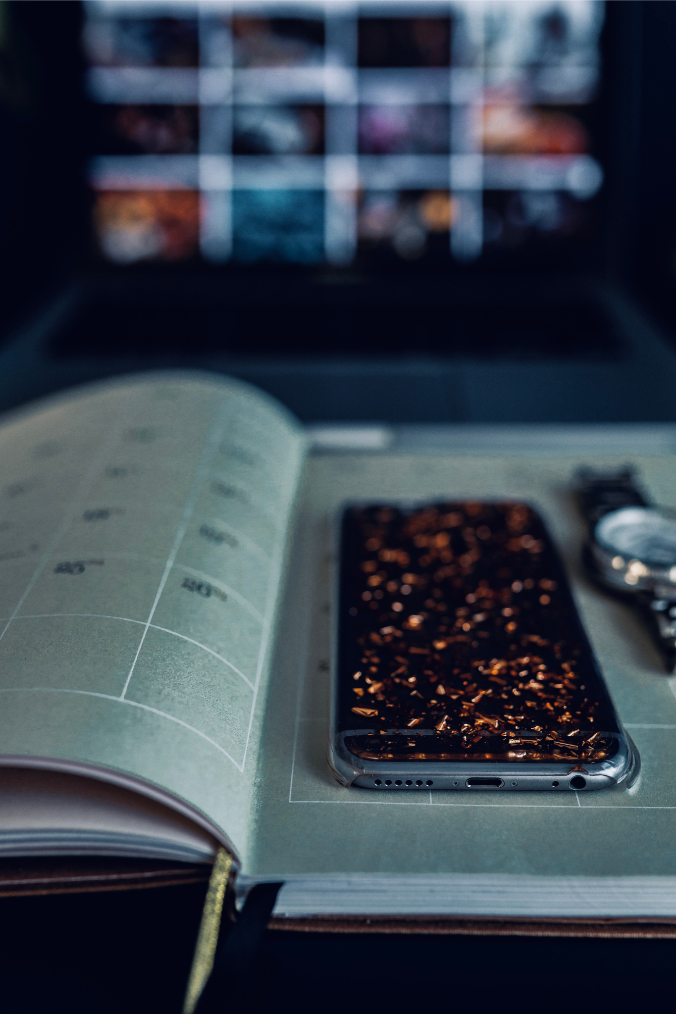 Dark room, open book, phone laying flat, computer screen in background,