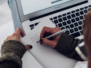 laptop, woman writing in notebook, social media strategy